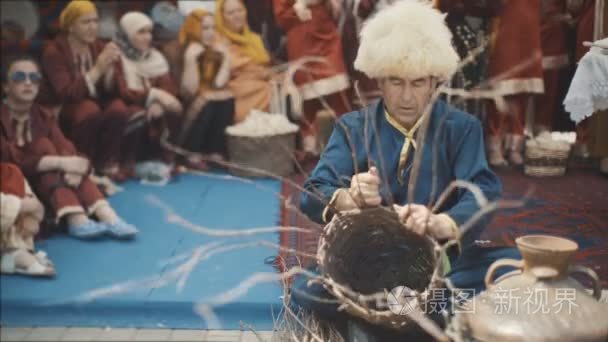 一个穿着民族服装的成年男子正在编织一个篮子。一个老正在织一篮子树枝。国庆节在东部。在山上有许多 ginshin 妇女视频
