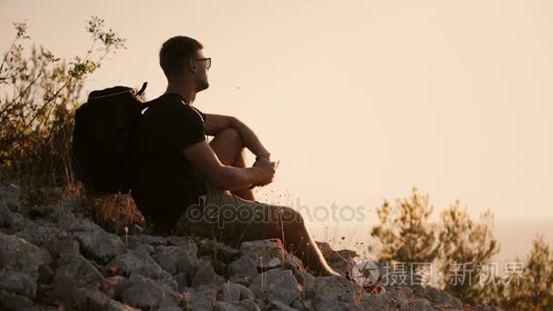 一个背着大背包的人在日落时坐在山上