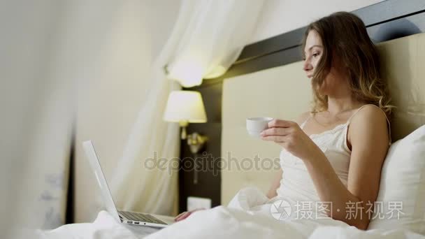 女人在她的笔记本电脑上聊天  在床上喝咖啡