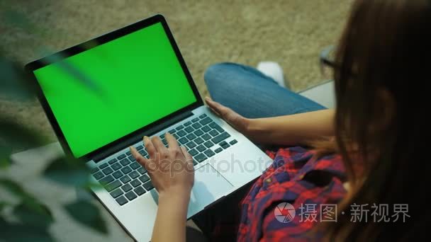 在起居室的沙发上, 年轻女子在笔记本电脑键盘上打字, 屏幕上有绿色。射过肩膀色度键