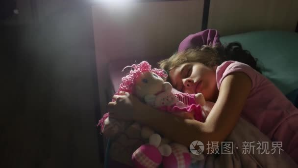可爱的小女孩晚上睡在沙发床上  抱着她的娃娃。在床上睡的女孩可爱的黑发的少女