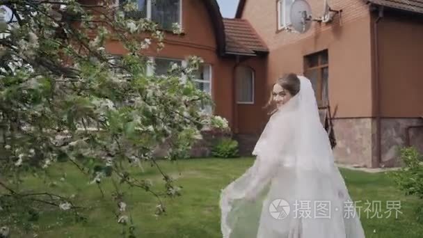 快乐的新娘穿着白色的长裙  在清晨的欢乐中漫步在苹果园的一个私人家中。婚礼日