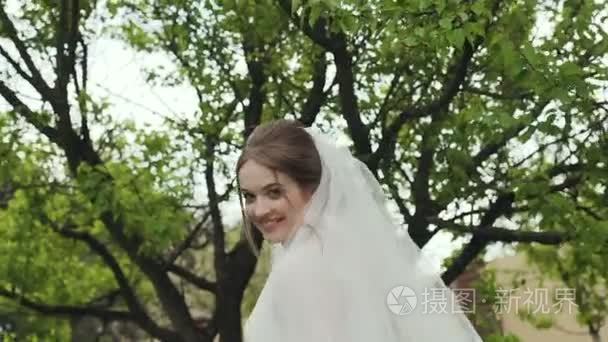 近距离模特的新娘微笑着进入相机  穿着白色的礼服在一个长花边。小女孩在绿色花园散步。婚礼日