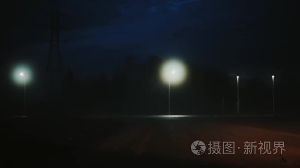 一辆汽车来到了大气漆黑的夜间公路。美丽的神秘电影拍摄。风景秀丽的天空。散城市灯