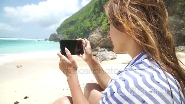美丽的妇女拍照使用手机在巴厘岛海滩印尼