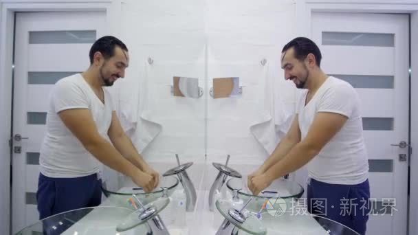 人在镜子前洗手。穿着白色 t恤衫的疲惫无胡子的家伙