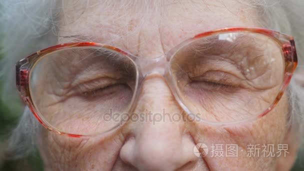 戴眼镜的老妇人在看镜头。一个老妇人的眼睛  周围有皱纹。关闭祖母的画像。慢动作