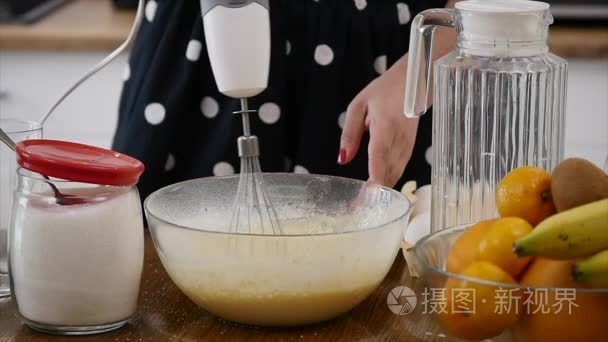 年轻女子准备面团混合配料在碗里用搅拌器在厨房。自制的食物。Slowmotion 射击