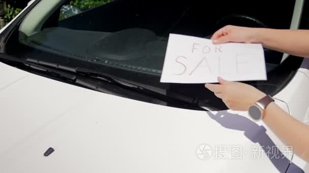 慢镜头的年轻女子在她的车上出售标志雨刷下的挡风玻璃