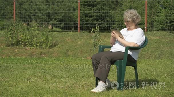 老女人抱着一个银电脑平板户外视频