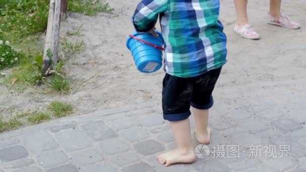 在公园的沙箱里背着塑料桶和铲子的赤脚学步男孩的慢动作镜头