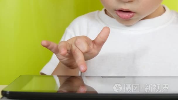 坐在桌旁的小男孩触摸着平板电脑的电子显示屏。特写