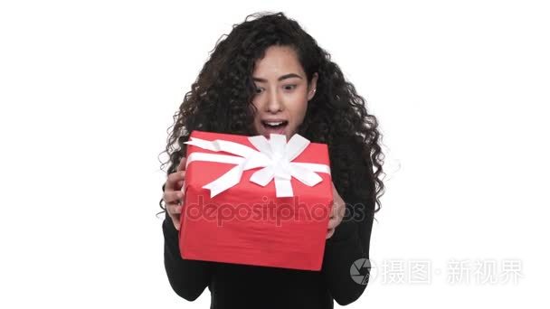 好奇的女性的画像20s 摇晃的红色箱子 gift-wrapped 激动和惊奇得到生日礼物在白色墙壁。情感的概念