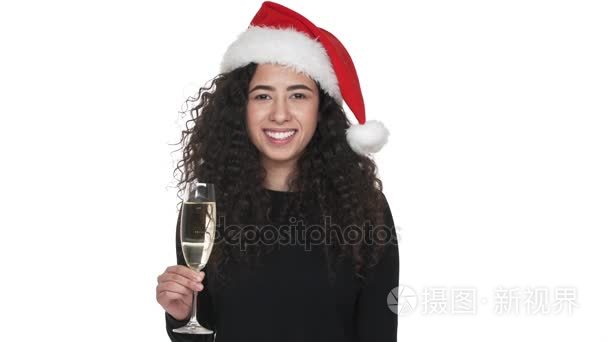 美丽的女人的肖像快乐  而庆祝新年穿着圣诞老人红帽喝香槟在白色的墙壁。情感的概念