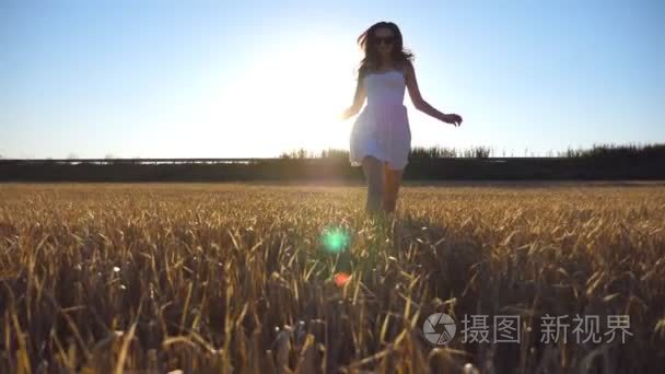 年轻美丽的女孩运行在麦田与太阳耀斑的背景。白种女人在美丽的草地上慢跑到镜头前。前视图慢动作关闭