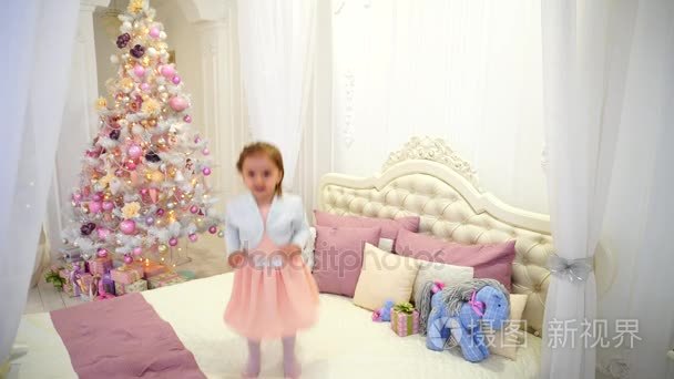 逗人喜爱的婴孩乐趣和跳跃在儿童房间在粉红色背景圣诞树与玩具