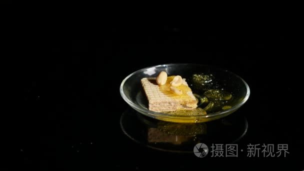 手拿着蜂蜜和坚果的华夫饼在一个黑色的背景碗里