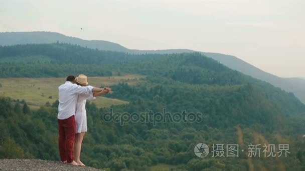 该名男子握着手  拥抱美丽的金发女郎回来  而站在山的边缘  享受风景