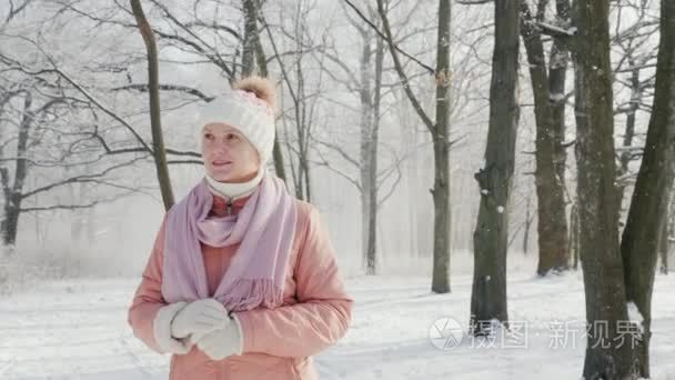 一个穿着粉红色夹克的女人在冬天的公园里散步。它在下雪  一个美丽晴朗的日子