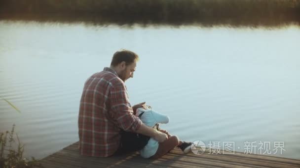 带着小男孩的白种人坐在湖边的码头上。父子一起。幸福的关系。养育孩子4k