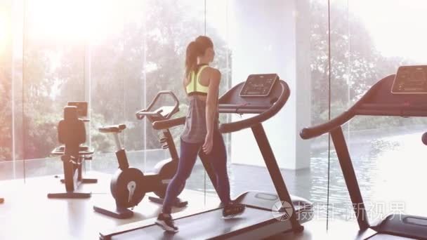 在一个全景窗口和太阳升起在健身房的早晨在跑步机上行走的妇女。健康生活方式的概念