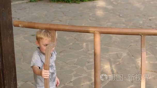 小男孩爬上公园凉亭的篱笆视频