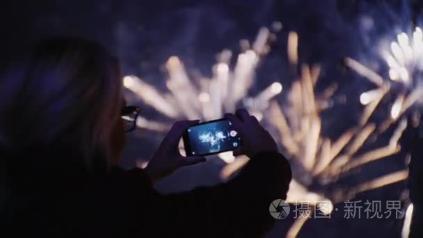 一个女人在夜空中拍摄烟花的照片。使用智能手机