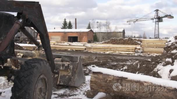 挖掘机在木工堆场堆放的木材材料覆盖在雪地上