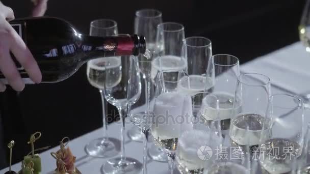 侍者把香槟倒入杯子里。桌面上满是闪闪发光的白葡萄酒和瓶子的背景