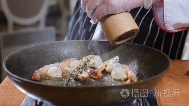 在平底锅上准备火烧风格菜的厨师的关闭。慢动作油和酒精点燃明火。烹调和添加胡椒粉到虎虾。4k 拍摄