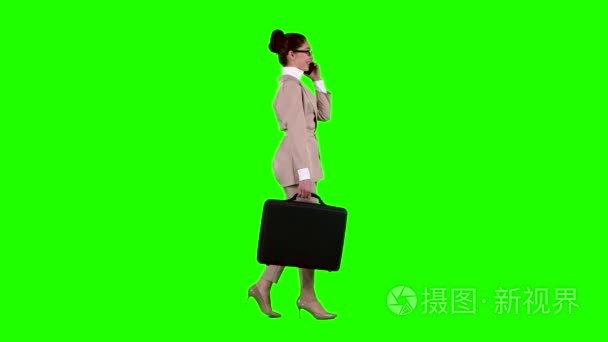 手里拿着箱子的商务女士在电话上讲话。绿色屏幕。侧面视图