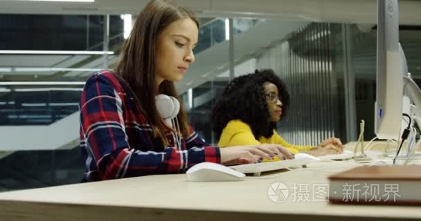 混合种族的肖像拍摄年轻女性在大的现代办公室的电脑上一起工作。在晚上。内