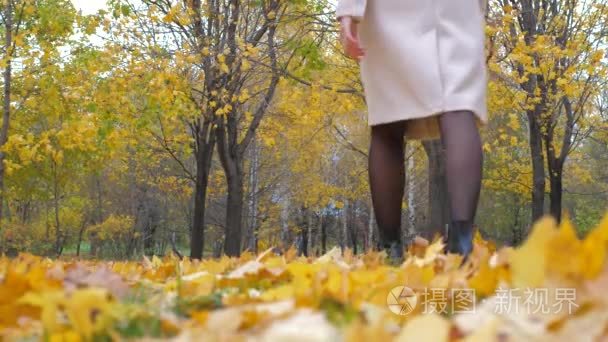 米色外套和橙色围巾的夫人走在秋天的黄叶子地毯4k