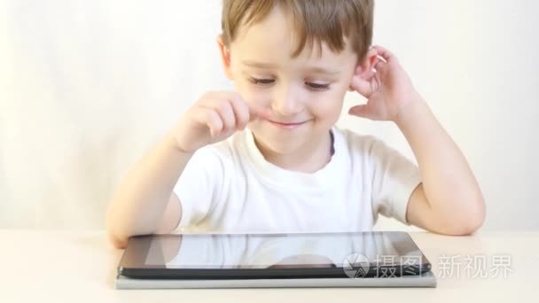 一个快乐的孩子坐在桌子上  在他脸上露出笑容的平板电脑上玩耍。这个孩子在玩电子游戏。儿童发展的概念