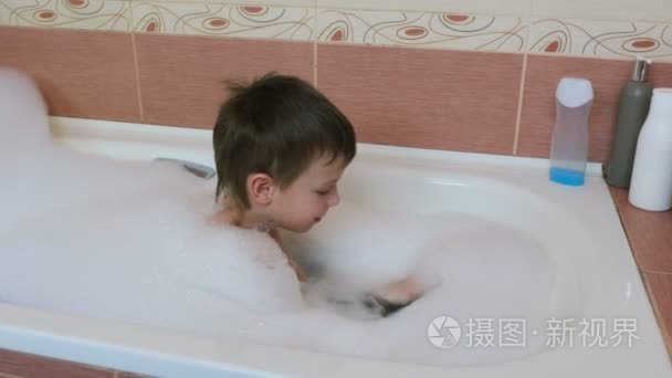 男孩67 在浴缸里玩白色泡沫。拿起泡沫, 戴上他的头