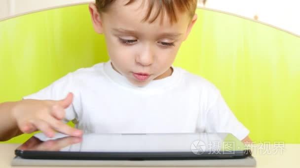 一个快乐的小男孩坐在桌子上, 触摸平板电脑的电子显示屏。一个孩子在玩笔记本电脑, 微笑着