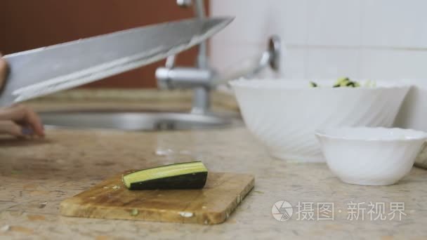 在厨房餐桌上的切割板上  手上切黄瓜的女人的特写。敲刀
