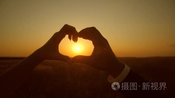 手在火热的日落太阳上显示心脏  爱的夫妇看日落