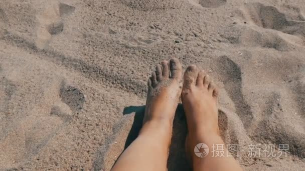 女性晒黑的腿和手指移动反对沙子的背景在海滩上