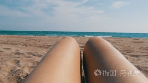 女子腿在沙滩上日光浴  背景是沙子和蓝色的海浪。女人裸脚在海滩上