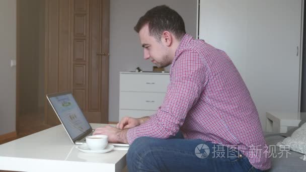 男子在家工作, 使用顶部和触控板。年轻的商人坐在桌边喝咖啡, 在电脑上工作。4k视频