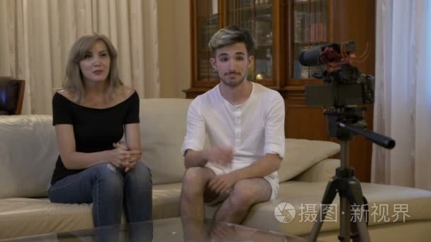 快乐微笑的年轻夫妇与相机录制视频消息沃客在家中的沙发上