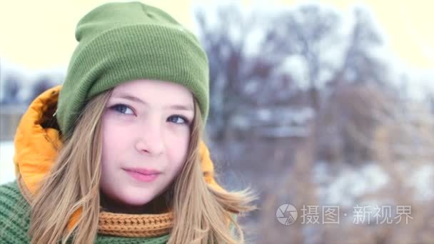 一个年轻美丽的少女的肖像, 金色的头发, 周围的雪, 女孩与绿色和棕色的围巾在绿色的时髦帽子, 微笑着, 环顾四周不同的方向。慢视频