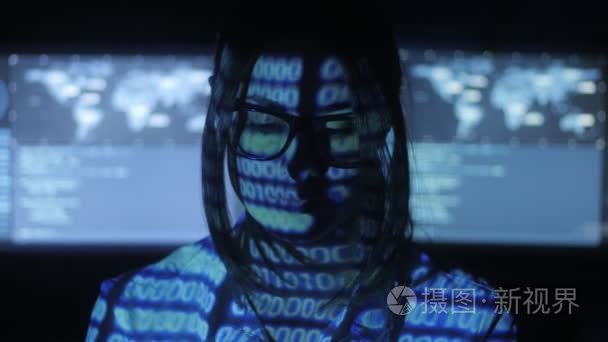 戴眼镜的女黑客程序员正在电脑上工作, 在网络安全中心装满了显示屏。她脸上的二进制代码