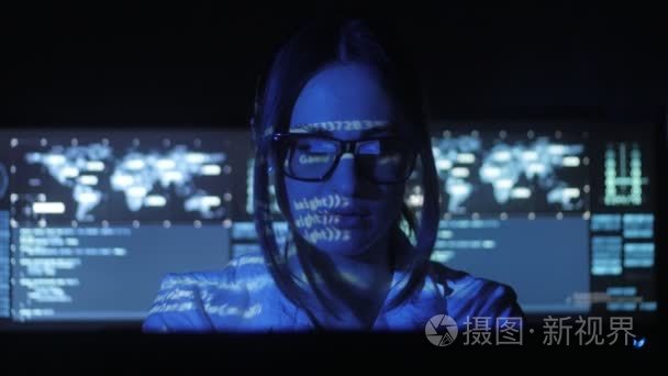 戴眼镜的女黑客程序员正在电脑上工作, 在网络安全中心装满了显示屏。她脸上的二进制代码