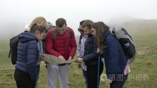 专业导游男士用背包阅读纸质地图和引领登山路线向年轻游客讲解路线