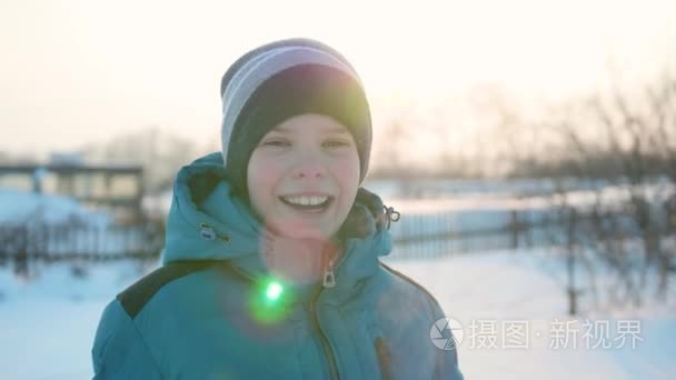 一个十几岁的少年在冬日公园里面带微笑。日落的时间。走在露天。健康的生活方式