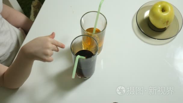 一个可爱的小女孩坐在桌子旁, 选择喝什么, 可乐或果汁, 健康生活方式的概念。