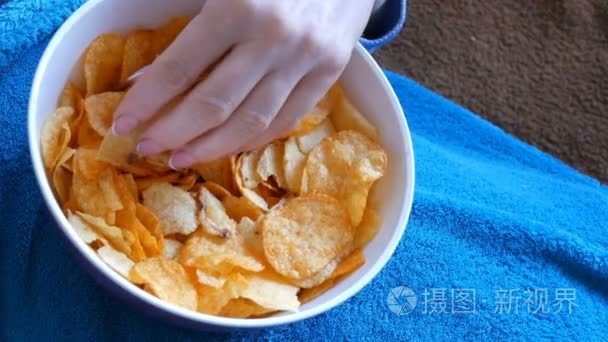 女人躺在沙发下的蓝色毯子, 吃薯片从一个深盘子.