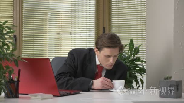 穿着西装的年轻人坐在办公室里, 在笔记本电脑上工作, 不喝可口的咖啡, 做鬼脸。在办公室工作。60 fps视频